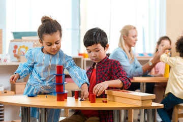 Selective focus of kids folding educational game with teacher and children at background in montessori school