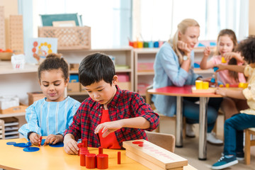 Selective focus of kids playing games with children and teacher at background in montessori school