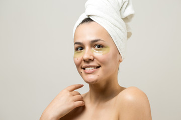 Young beautiful girl in a white towel on his head wears collagen gel patches under her eyes. Mask under eyes treatment face.