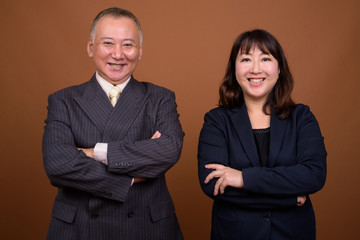 Happy mature Asian businessman and mature Asian businesswoman with arms crossed together