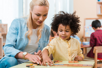 Selective focus of teacher helping to african american kid with wooden game in montessori class - Powered by Adobe