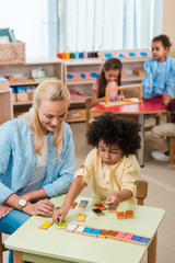 Selective focus of child playing game by smiling teacher with kids at background in montessori...