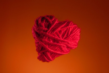 red heart made of knitted thread, valentines day. copy space. on an orange background