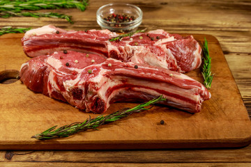 Raw fresh beef rib eye steaks on bone with spices and rosemary on wooden table