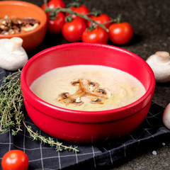 Bowl of mushroom cream soup with fried champignon mushrooms and vegetables on black stone background. Rustic style. Close up.