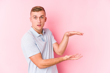 Young caucasian man isolated shocked and amazed holding a copy space between hands.