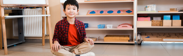 Panoramic shot of smiling asian kid sitting on floor in montessori school