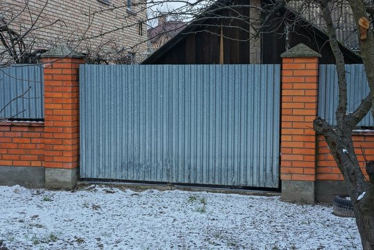 gray metal gate and part of a red brick fence in white snow on a winter street