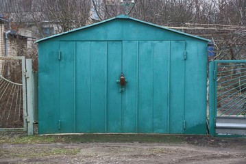 one large green iron garage with closed gates on a rural street with a fence