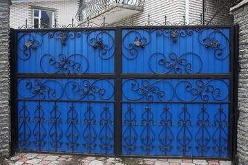 large closed colored gates of iron black forged bars in a pattern on a blue metal wall on the street