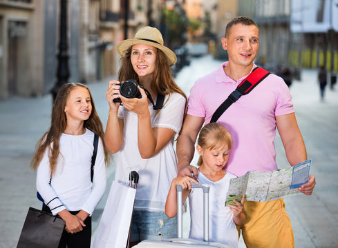 Tourist family using map and taking photo of city while strolling