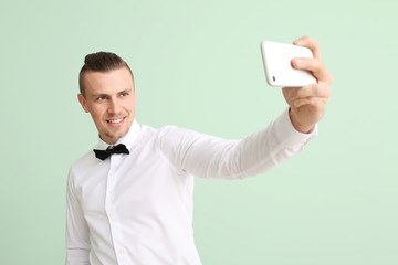 Handsome young man taking selfie on color background