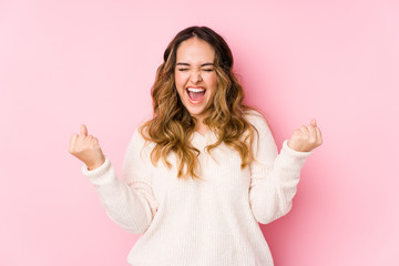 Young curvy woman posing in a pink background isolated cheering carefree and excited. Victory...