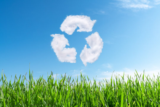 Clouds on the blue sky in shape of the symbol of recycling on green background. Protection nature and future concept.