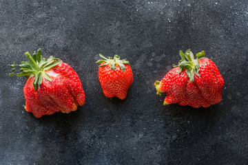 Ugly three ripe organic strawberry on black background.