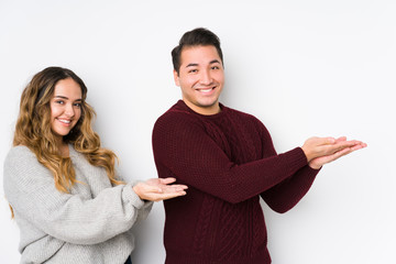 Young couple posing in a white background holding a copy space on a palm.