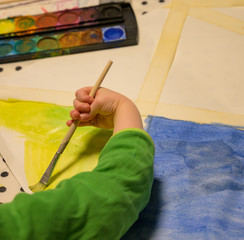 Kind malt mit einem Pinsel und Tusche bunte Formen auf einem Blatt