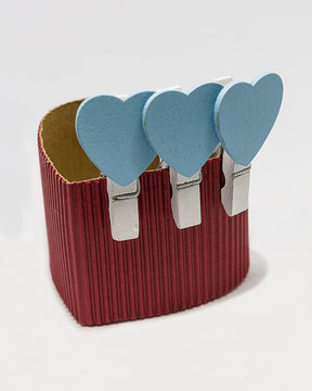 Caja de cart&oacute;n corrugado rojo en forma de coraz&oacute;n con pinzas blancas de corazones azules.