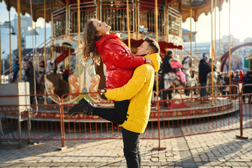 young romantic couple in love wearing in bright yellow and red down jackets walking city, hugging...