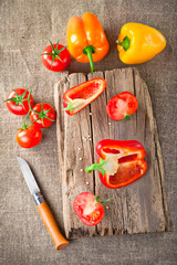 Fresh tomato, paprika, steel knife and vintage wooden cutting board on canvas tablecloth
