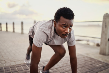 Fototapeta premium Portrait of a young african american male athlete in start position preparing for running along sea