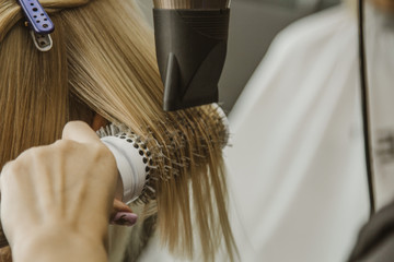Naklejka premium Close up of hairdresser hands drying human hair with equipment. Woman holding a comb. close-up. Macro photo.