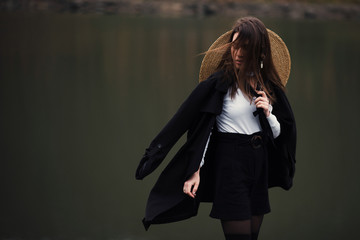 Portrait of young brunette with straw hat. Woman posing near lake and enjoying nature views in...