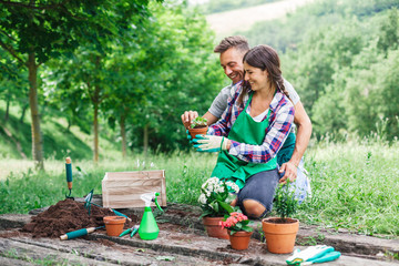 Young loving couple have fun with gardening work on a wooden floor during spring day - Millennial are dressed with green aprons - 317499290