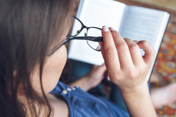 A woman with vision problems is reading a book with glasses.