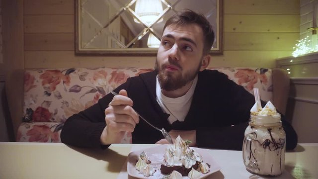 Bearded guy eating dessert cake with a spoon in a shabby cafe. enjoyment and relaxation
