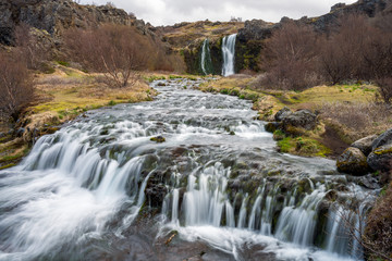 Fototapeta na wymiar Waterfall cascade in the area of Gjain in Porsdalur in the Icelandic highlands. Overcast sky. Long exposure shot of the river. Travling concept.