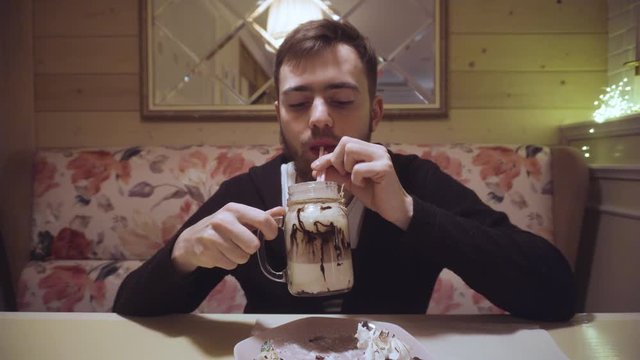 Bearded guy drinking a milkshake from a straw in a shabby cafe