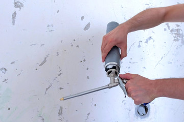 Man construction worker screws a bottle of mounting foam to tool, hands closeup. Man preparing construction foam for work. Bottle of spray with mounting foam and instrument for repair room.