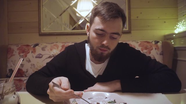 bearded guy eating delicious cheesecake in a restaurant enjoying. small spoon with cream