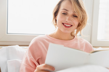 Woman indoors at home lies in bed reading book.