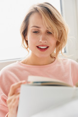 Woman indoors at home lies in bed reading book.