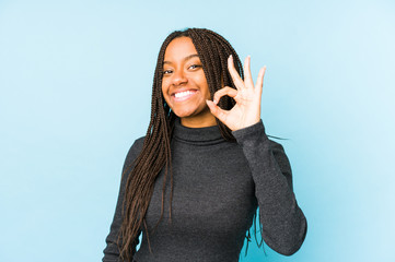 Young african american woman isolated on blue background cheerful and confident showing ok gesture.