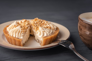 Cut cake basket with caramel near cappuccino on black wooden background.