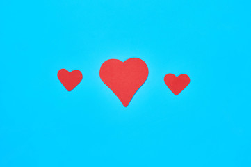 Fototapeta na wymiar Three small and big red paper hearts on blue background. Concept of Valentines Day. Top view. Close-up