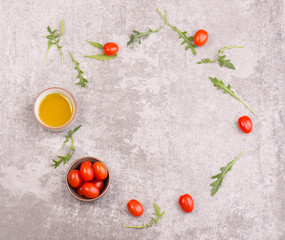 Red cherry tomatoes, fresh arugula leaves and olive oil on a grext stone textured background, empty copy space