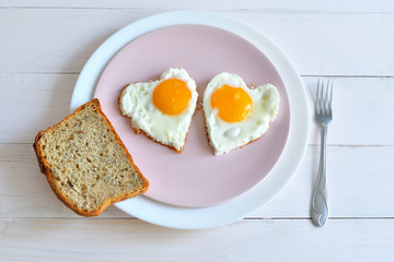 Two fried eggs on pink plate for healthy breakfast on wooden table. top view