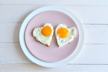 Two fried eggs on pink plate for healthy breakfast on wooden table. top view
