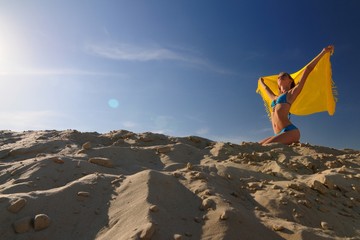Fototapeta na wymiar Young woman in bikini standing on sand and holding yellow pareo