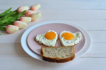 Breakfast on Valentine's Day - fried eggs in the shape of a heart and bouquet of pink tulips.top view