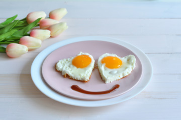 Breakfast on Valentine's Day - fried eggs in the shape of a heart and bouquet of pink tulips.top view