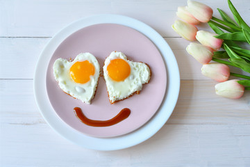 Breakfast on Valentine's Day - fried eggs in the shape of a heart and bouquet of pink tulips.top view