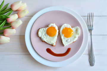 Breakfast on Valentine's Day - fried eggs in the shape of a heart and bouquet of pink tulips.top view