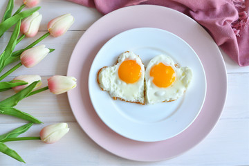 Breakfast on Valentine's Day - fried eggs in the shape of a heart and bouquet of pink tulips.top view