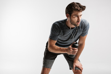 Image of young unshaven man using earphones and holding water bottle