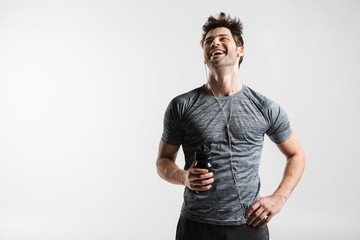 Image of young laughing man using earphones and holding water bottle